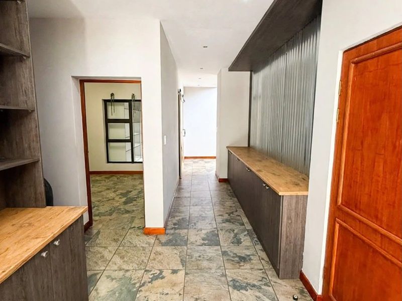 A spacious hallway featuring stone tile flooring, built-in cabinetry with timber countertops, and modern recessed lighting, leading to adjacent rooms.