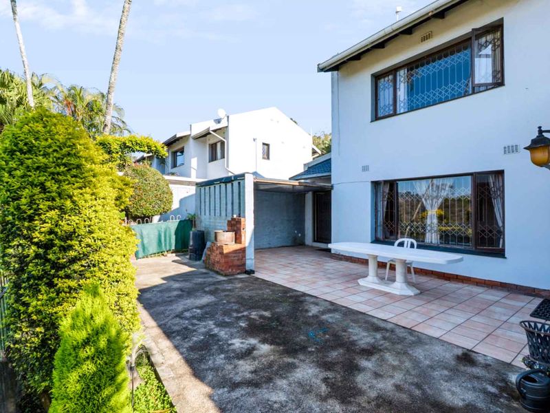 Rear exterior view of the townhouse featuring a tiled patio area, concrete paving, and a built-in brick braai.