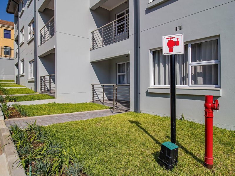 Exterior view of an apartment building featuring ground-floor balconies, a paved walkway, landscaped lawn, and a fire hydrant.