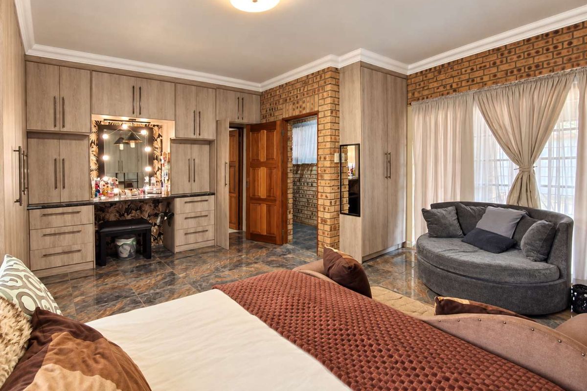 Spacious bedroom featuring extensive built-in cabinetry, a dedicated vanity area, exposed brick accents, and polished tiled flooring.