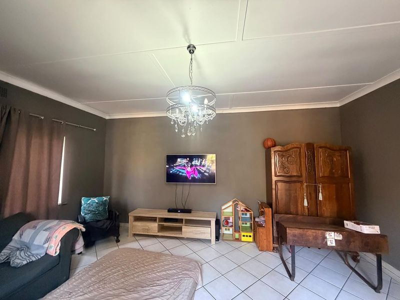 A living room featuring tiled flooring, a central chandelier, and a wall-mounted television.