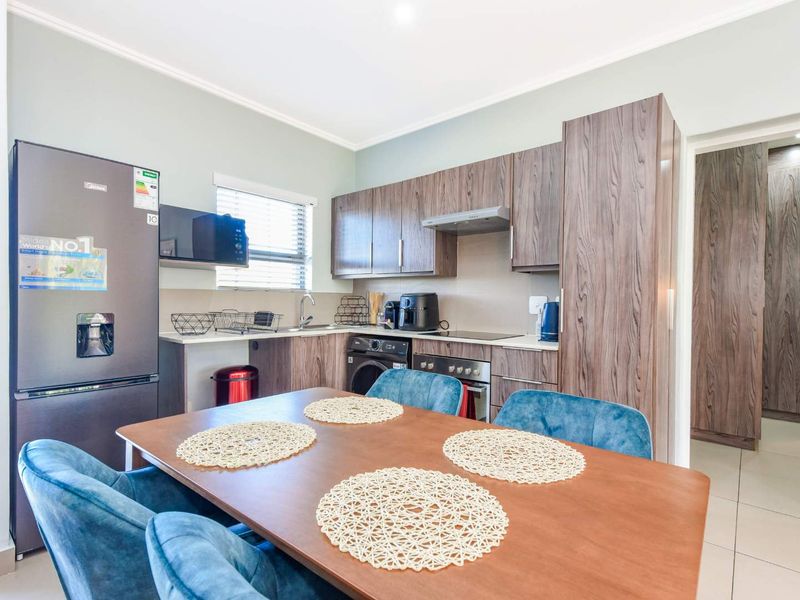 Modern open-plan kitchen featuring wood-grain cabinetry, integrated appliances, and tiled flooring, seamlessly flowing into the dining area.