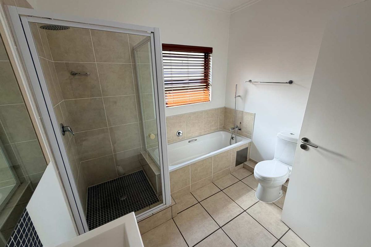A clean, functional bathroom featuring a separate glass-enclosed shower, a built-in bathtub with tiled surround, and a standard toilet.