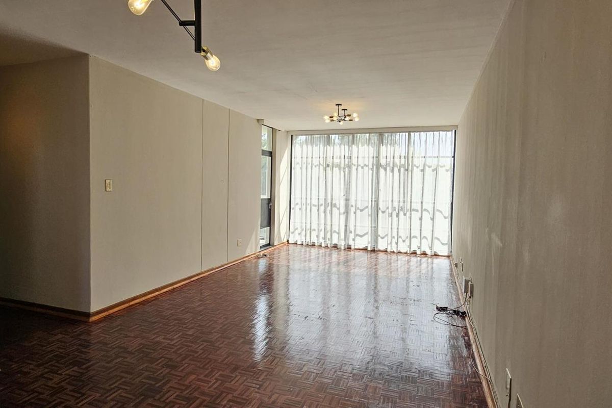An empty living room featuring polished parquet flooring and a large sliding glass door that provides natural light.