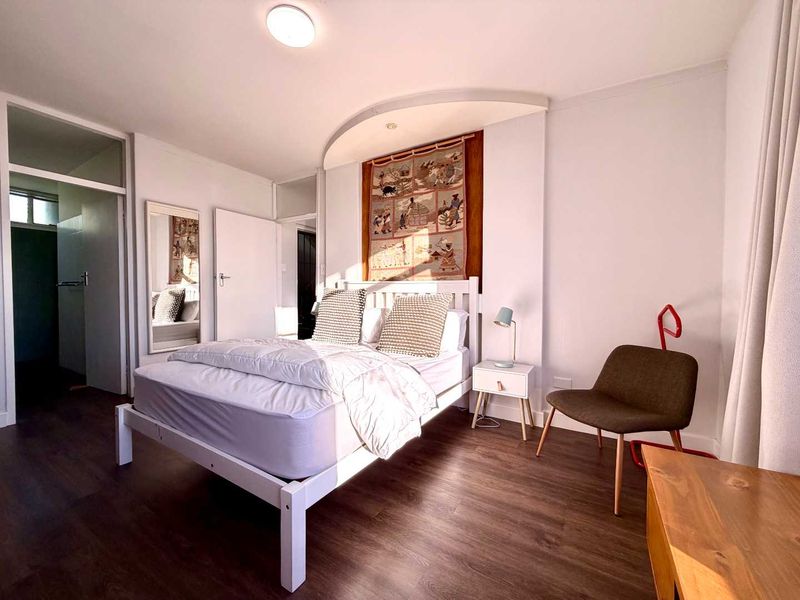A well-lit bedroom featuring laminate flooring, a recessed ceiling architectural detail, and neutral wall finishes.