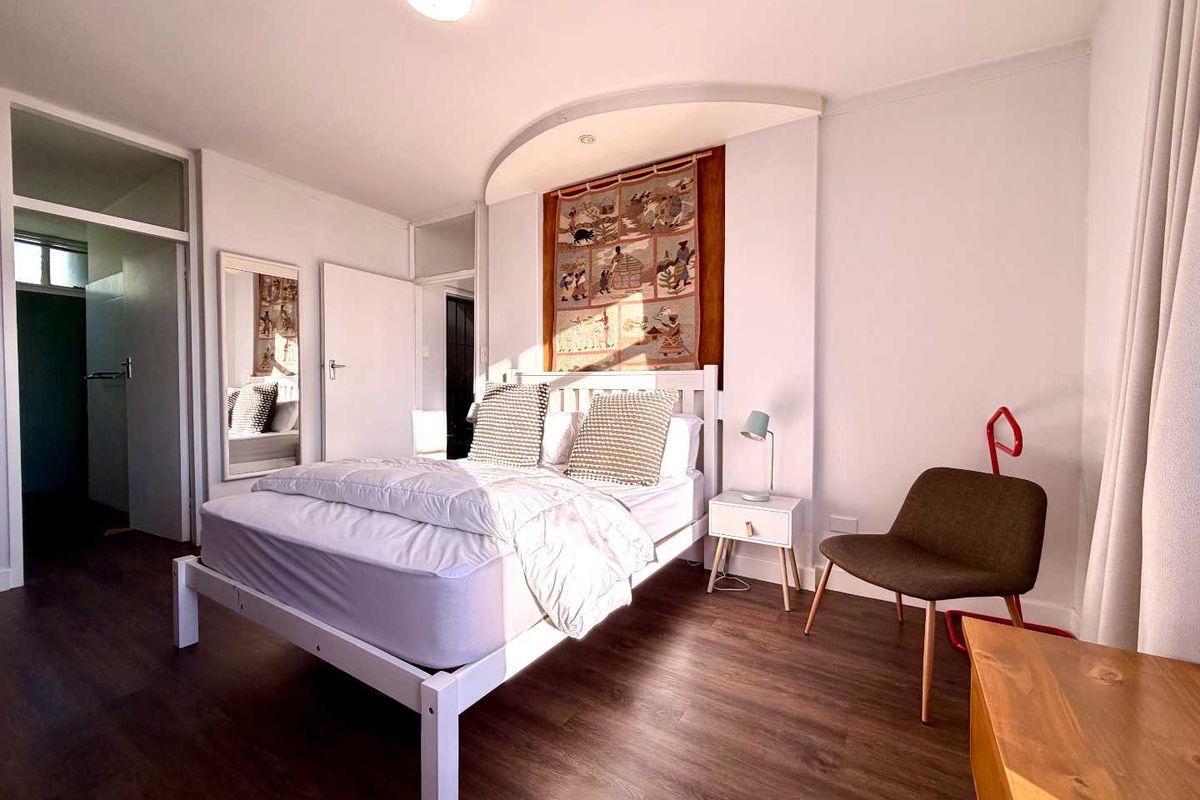 A well-lit bedroom featuring laminate flooring, a recessed ceiling architectural detail, and neutral wall finishes.