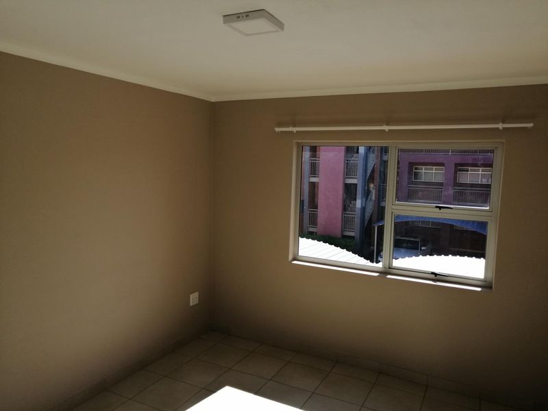 A clean, empty bedroom featuring neutral wall paint, tiled flooring, and an aluminium-framed window with a fitted curtain rod.