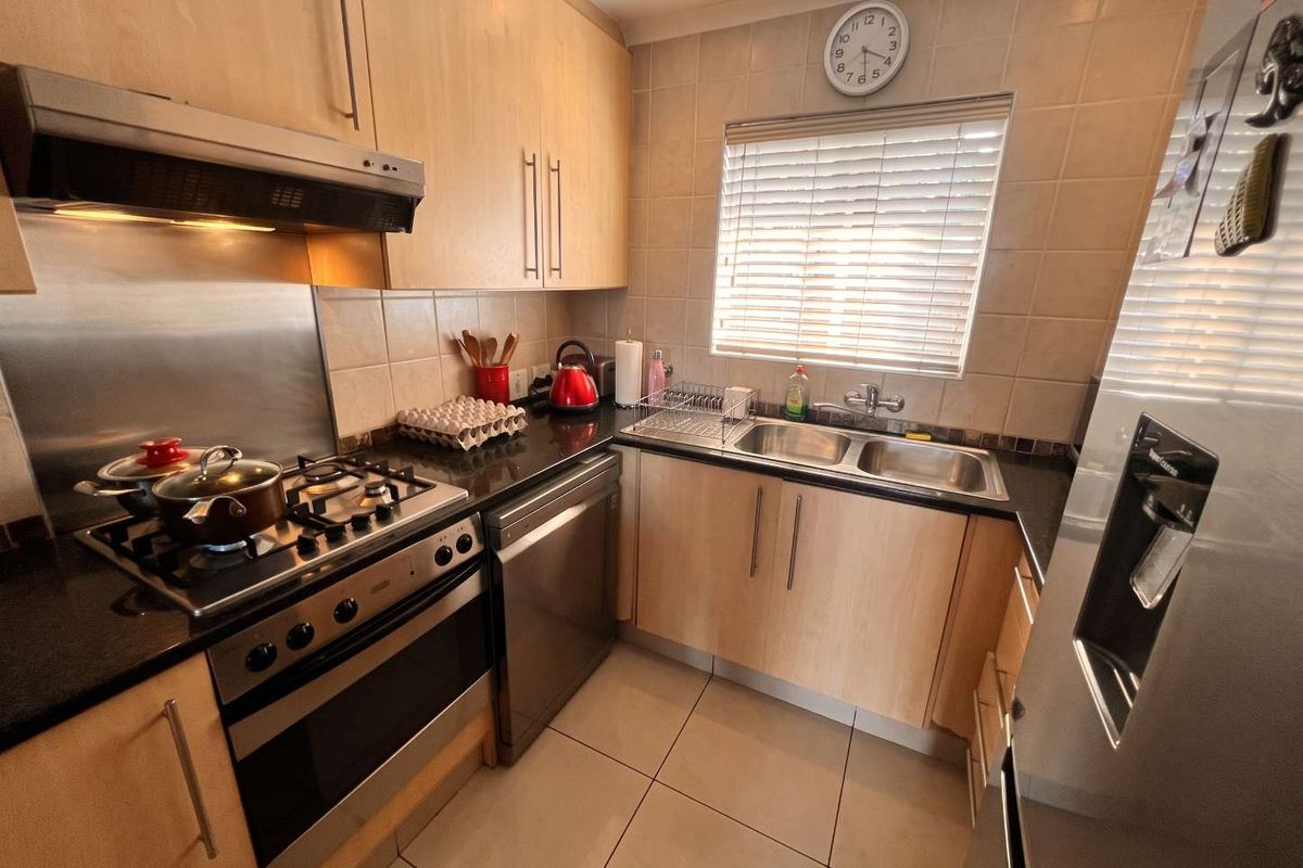 A functional kitchen featuring light wood cabinetry, granite countertops, a gas hob with extractor, and a double basin sink with tiled splashbacks.