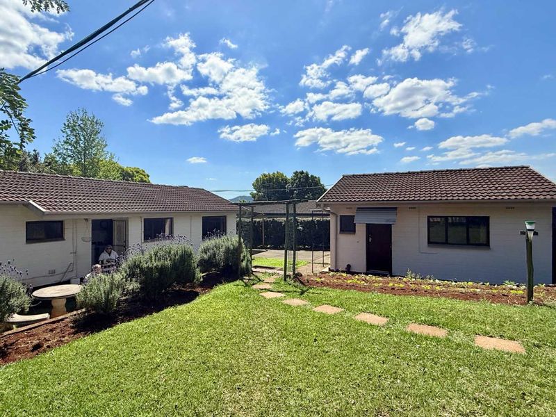 A view of the rear exterior of the house featuring a well-maintained lawn, stone pathway, and established garden beds against the building facade.