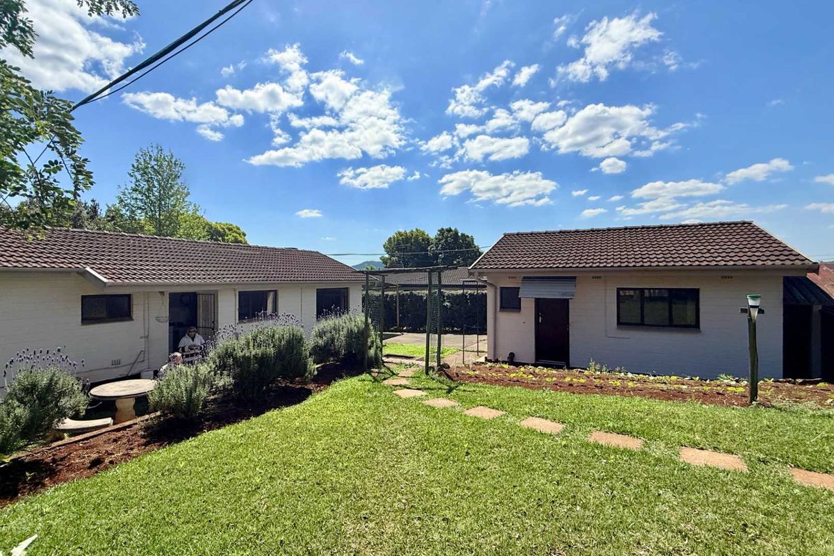 A view of the rear exterior of the house featuring a well-maintained lawn, stone pathway, and established garden beds against the building facade.