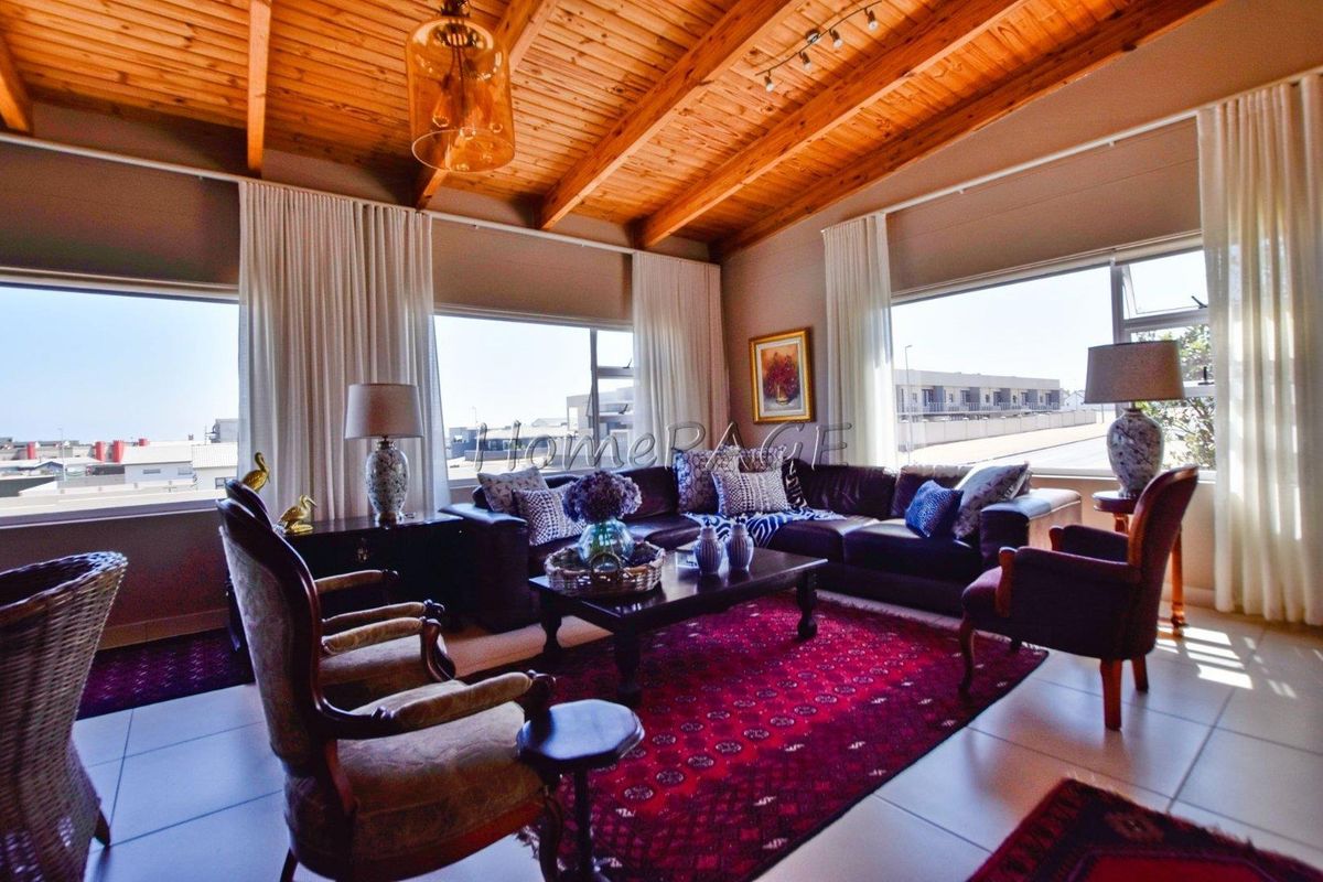 Spacious living room featuring high exposed timber beam ceilings, large windows providing ample natural light, and neutral tiled flooring.
