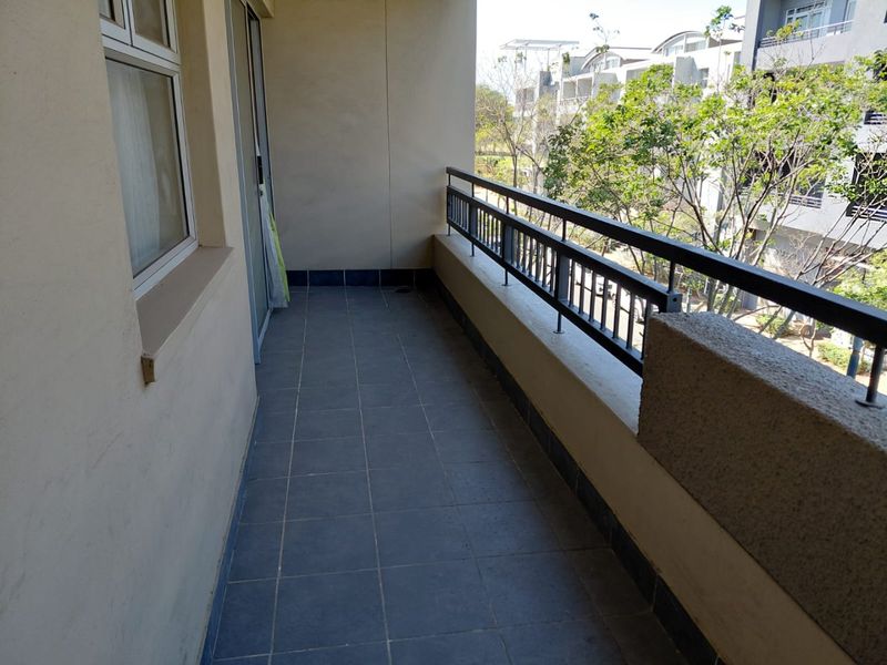 A private balcony featuring tiled flooring and a metal balustrade, offering an outdoor space accessible via a sliding glass door.