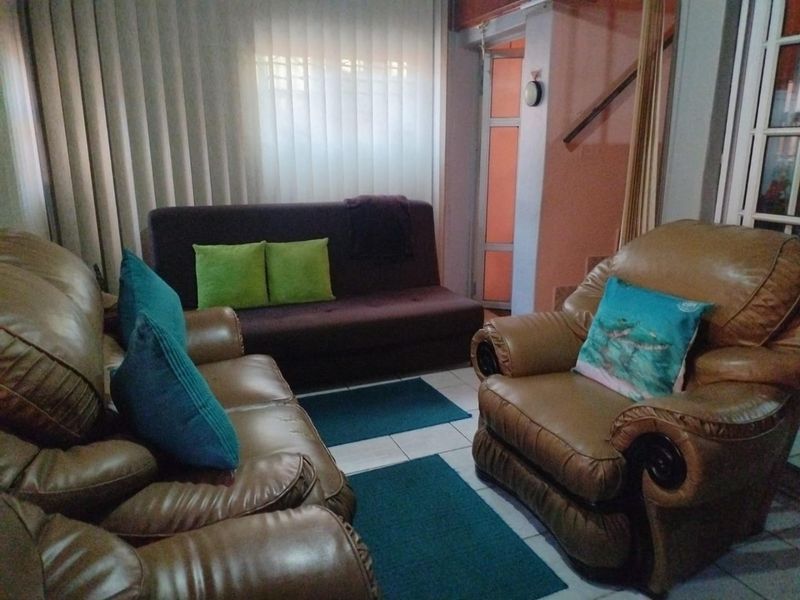 A living room area featuring tiled flooring, vertical window blinds, and access to a staircase.