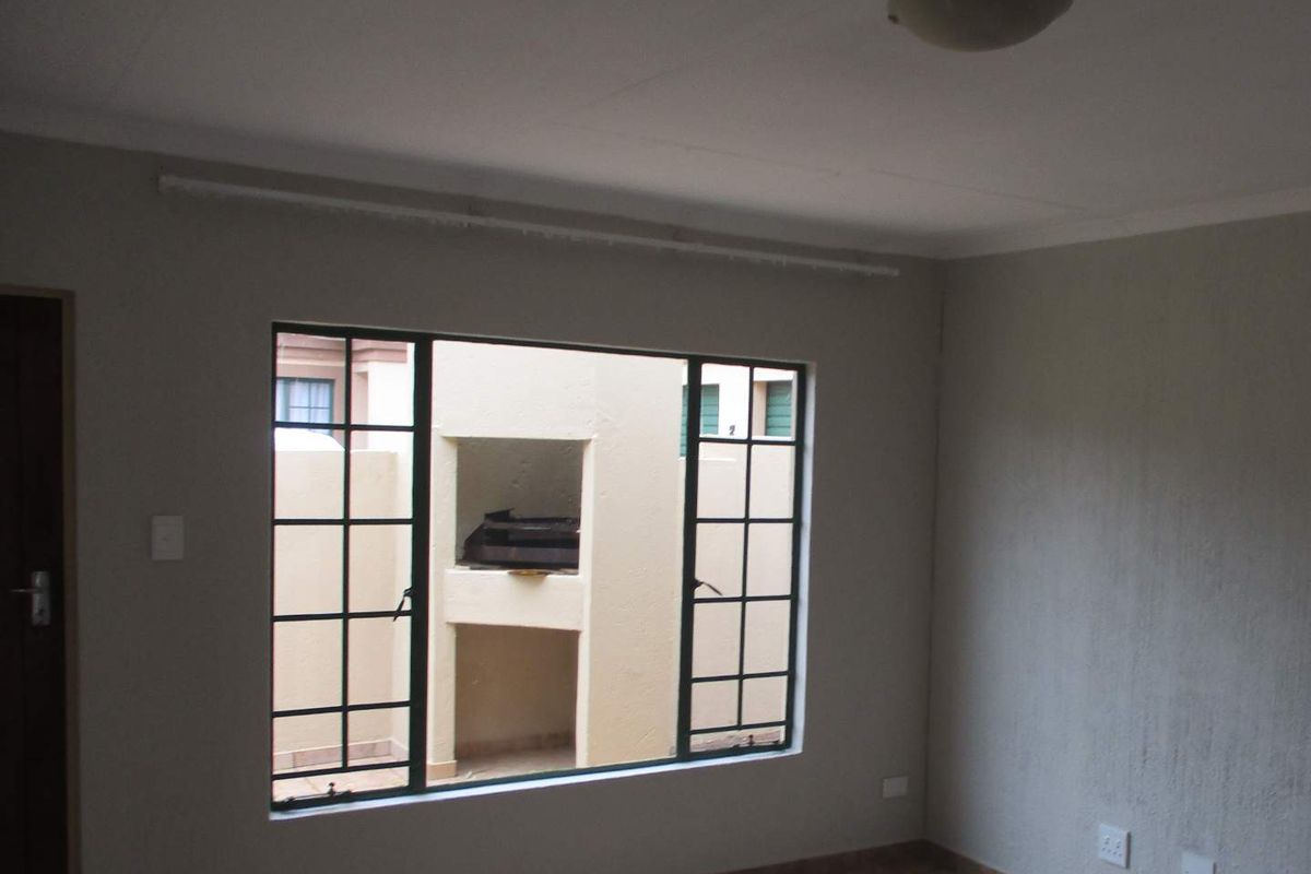 An empty living room featuring tiled flooring, a metal-framed window, and neutral wall finishes, offering a blank canvas for interior design.