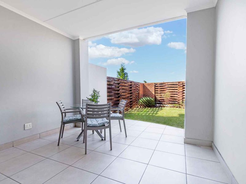 A covered patio featuring tiled flooring and a timber privacy screen, overlooking a private garden area.