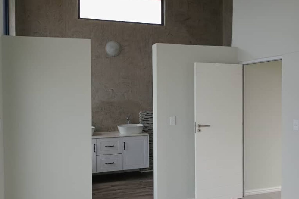 A modern bedroom interior featuring exposed timber ceiling beams, tiled flooring, and an en-suite bathroom area with a vanity and basin.