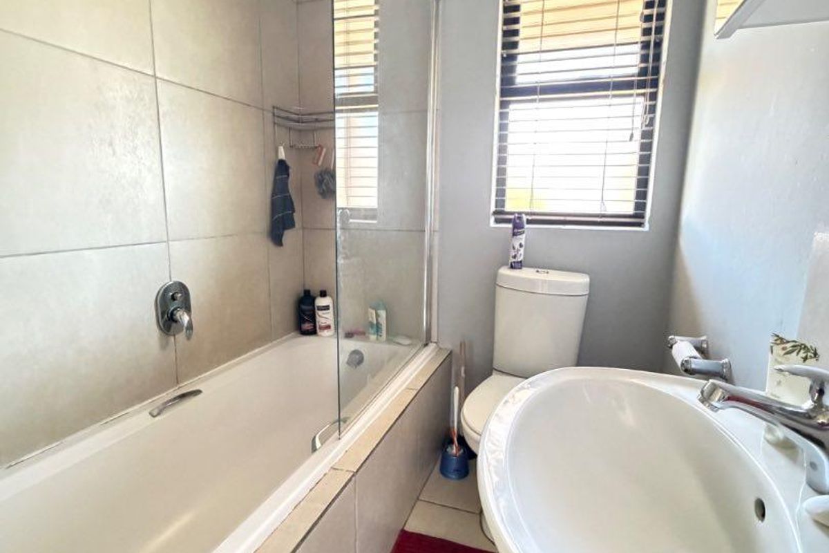 A functional bathroom featuring a bathtub with a glass shower screen, a pedestal basin, and a toilet, finished with neutral wall tiling.
