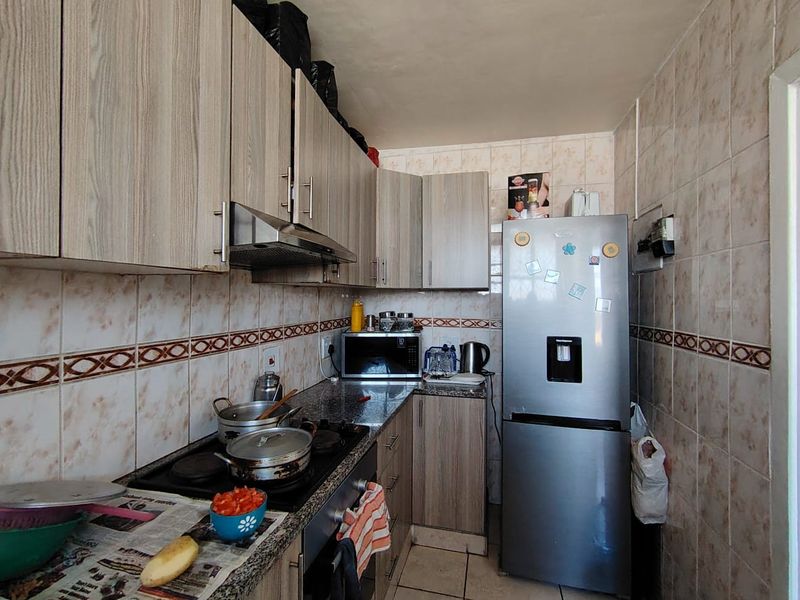Compact kitchen featuring wood-look cabinetry, granite countertops, a built-in hob with extractor fan, and full-height wall tiling.