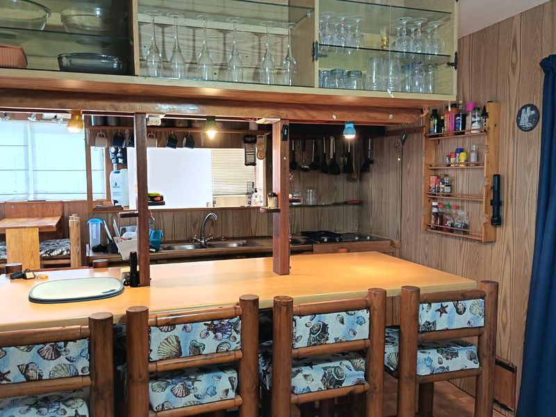 A dated kitchen featuring wood-paneled walls, built-in cabinetry, a double sink, and a breakfast bar with integrated storage and display shelving.