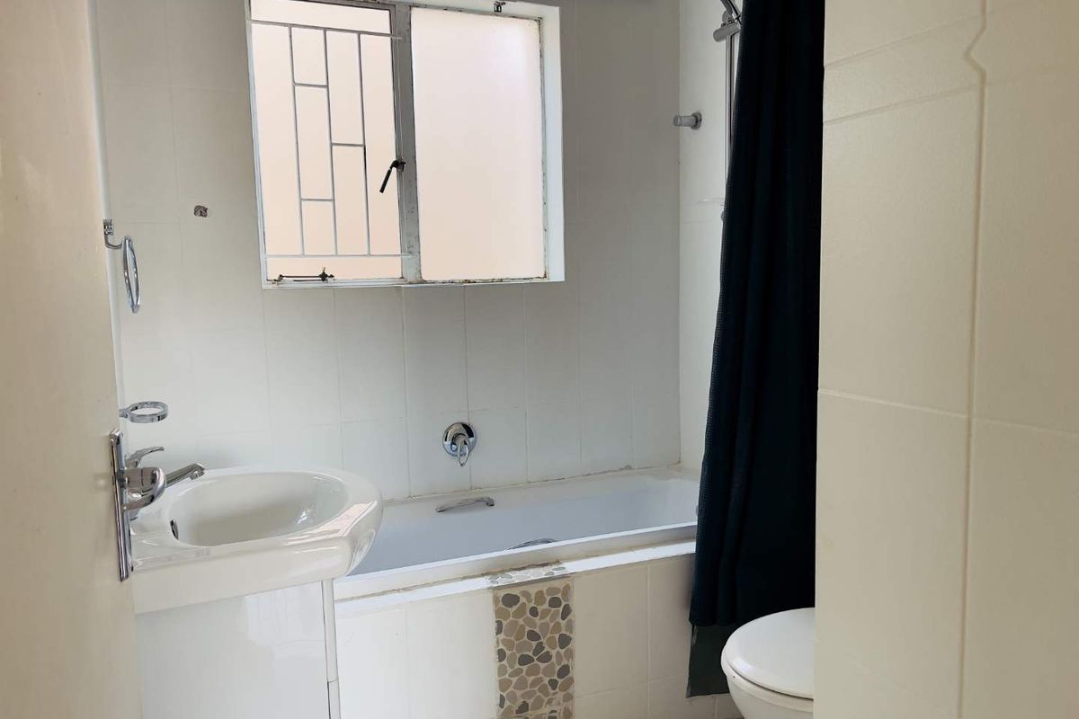 A functional bathroom featuring a pedestal basin, bathtub with shower attachment, and toilet, finished with white wall tiles and a decorative mosaic accent.