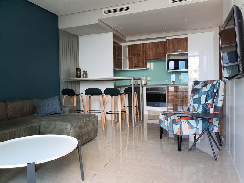 Modern open-plan living area featuring a sleek kitchen with built-in cabinetry, integrated oven, glass splashback, and a functional breakfast bar.