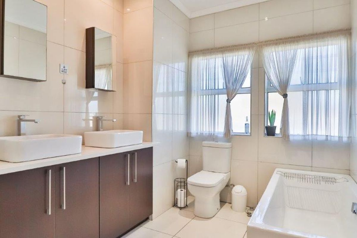 Modern bathroom featuring a double vanity with vessel sinks, built-in cabinetry, a bathtub, and tiled finishes throughout.