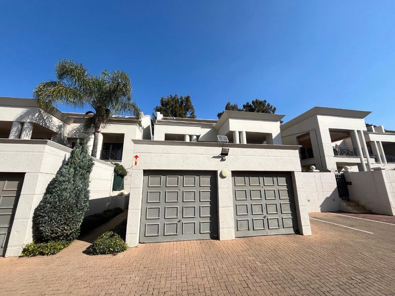 Front elevation of a townhouse complex featuring a double garage, paved driveway, and upper-level balconies with a modern textured finish.