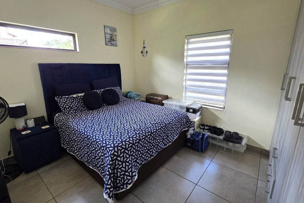 A functional bedroom featuring tiled flooring, built-in cabinetry, and a window fitted with a modern roller blind.