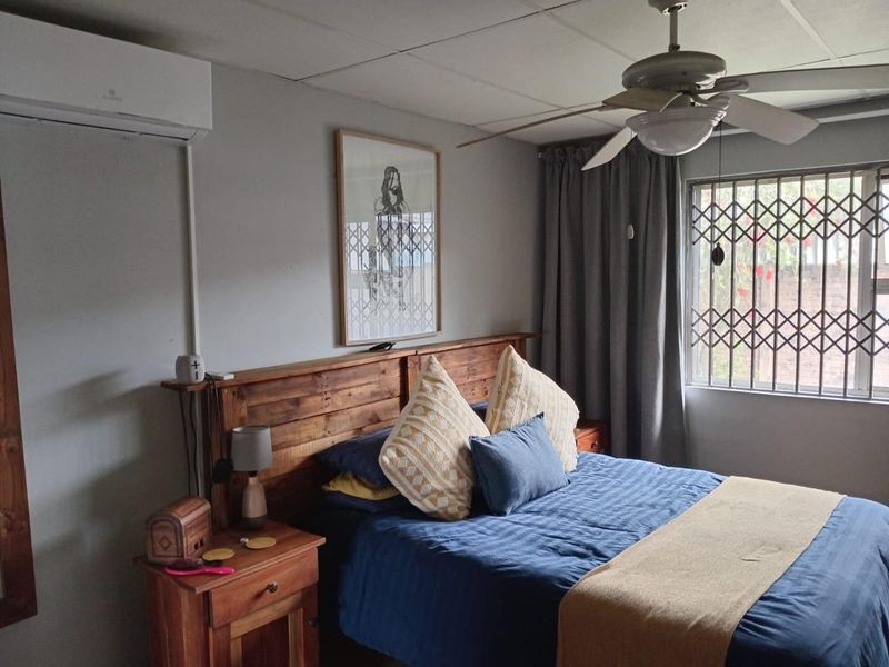 A functional bedroom featuring a ceiling fan, split-system air conditioning unit, and a window fitted with a security gate.
