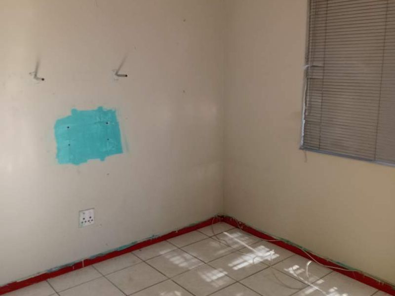 An empty bedroom featuring tiled flooring and venetian blinds, currently requiring wall repairs and cosmetic finishing to restore its condition.