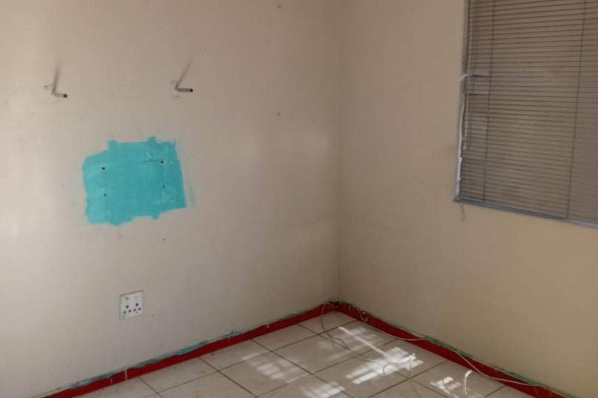 An empty bedroom featuring tiled flooring and venetian blinds, currently requiring wall repairs and cosmetic finishing to restore its condition.