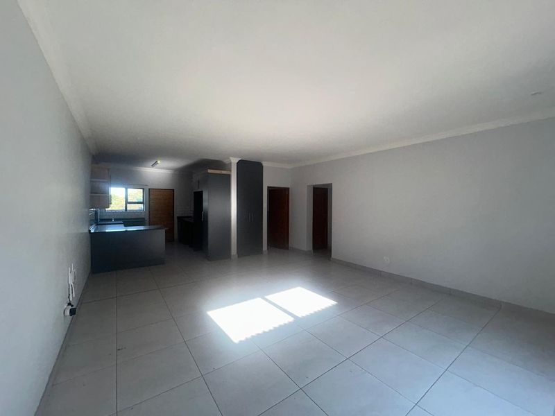 Spacious open-plan living area featuring neutral tiled flooring and an integrated kitchen with dark cabinetry, offering a versatile layout for modern living.