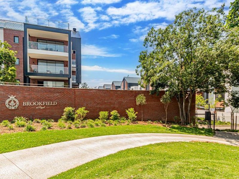 Front view of the Brookfield residential complex featuring a brick boundary wall, landscaped gardens, and modern multi-story townhouse architecture.