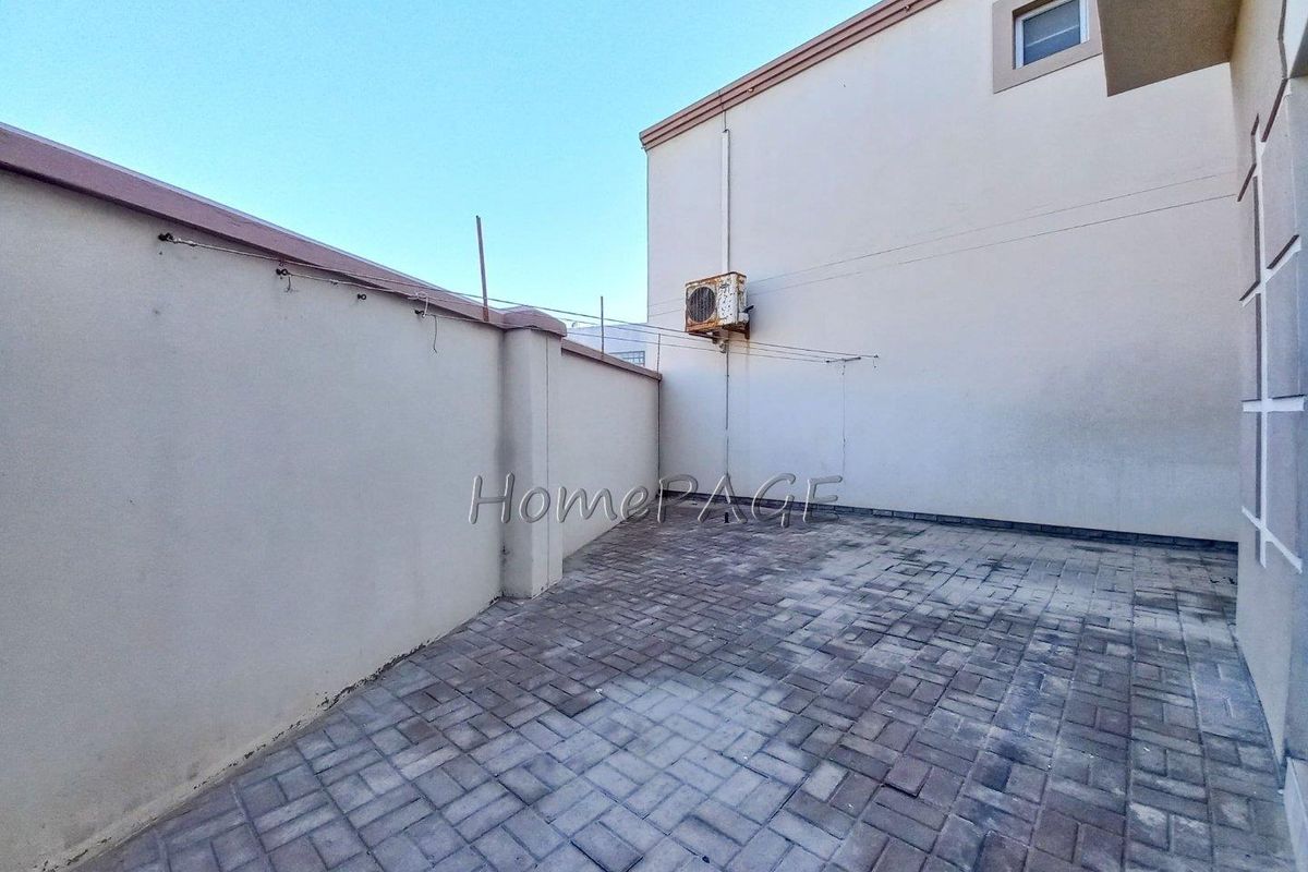 A paved rear courtyard area featuring a perimeter boundary wall and a wall-mounted air conditioning unit.