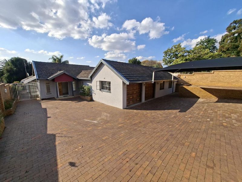 Front exterior view of the property featuring a spacious paved driveway, double garage, and a covered carport area.