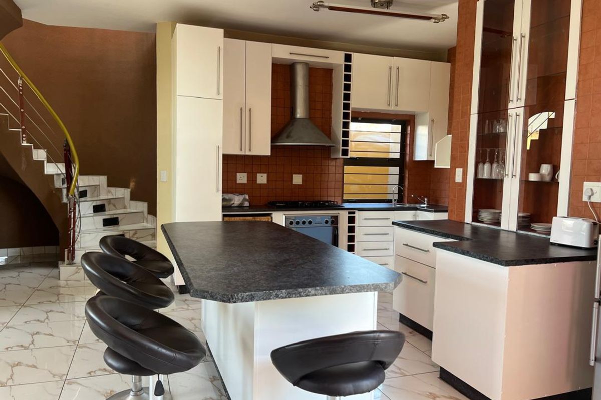 A functional kitchen featuring white cabinetry, dark countertops, a central island, and a built-in extractor fan, adjacent to a staircase with marble-look steps.