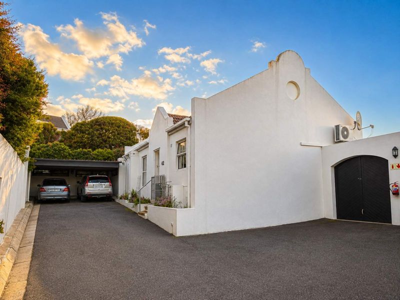 Front elevation of the townhouse featuring a paved driveway, covered carport, and secure garage access with exterior lighting and air conditioning unit.