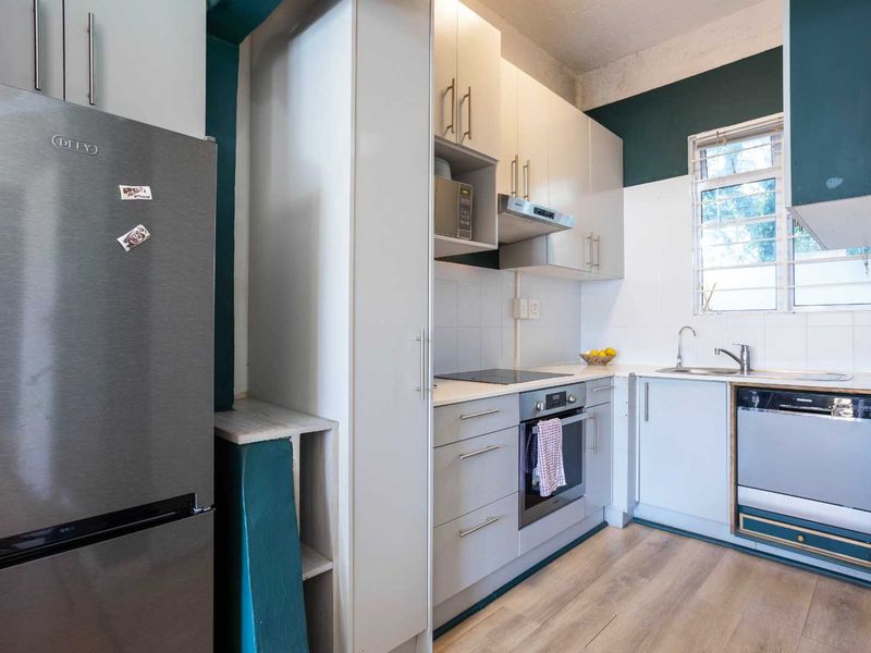 A functional kitchen featuring modern light-toned cabinetry, integrated appliances, a stainless steel sink, and a tiled backsplash with contrasting dark green wall accents.