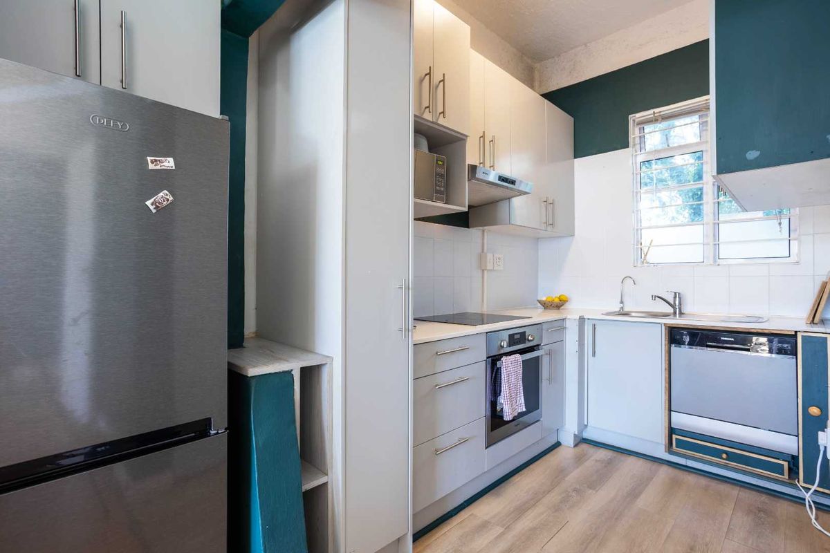 A functional kitchen featuring modern light-toned cabinetry, integrated appliances, a stainless steel sink, and a tiled backsplash with contrasting dark green wall accents.