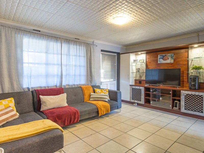 Spacious living room featuring tiled flooring, a built-in wooden entertainment unit with integrated shelving, and a textured ceiling finish.