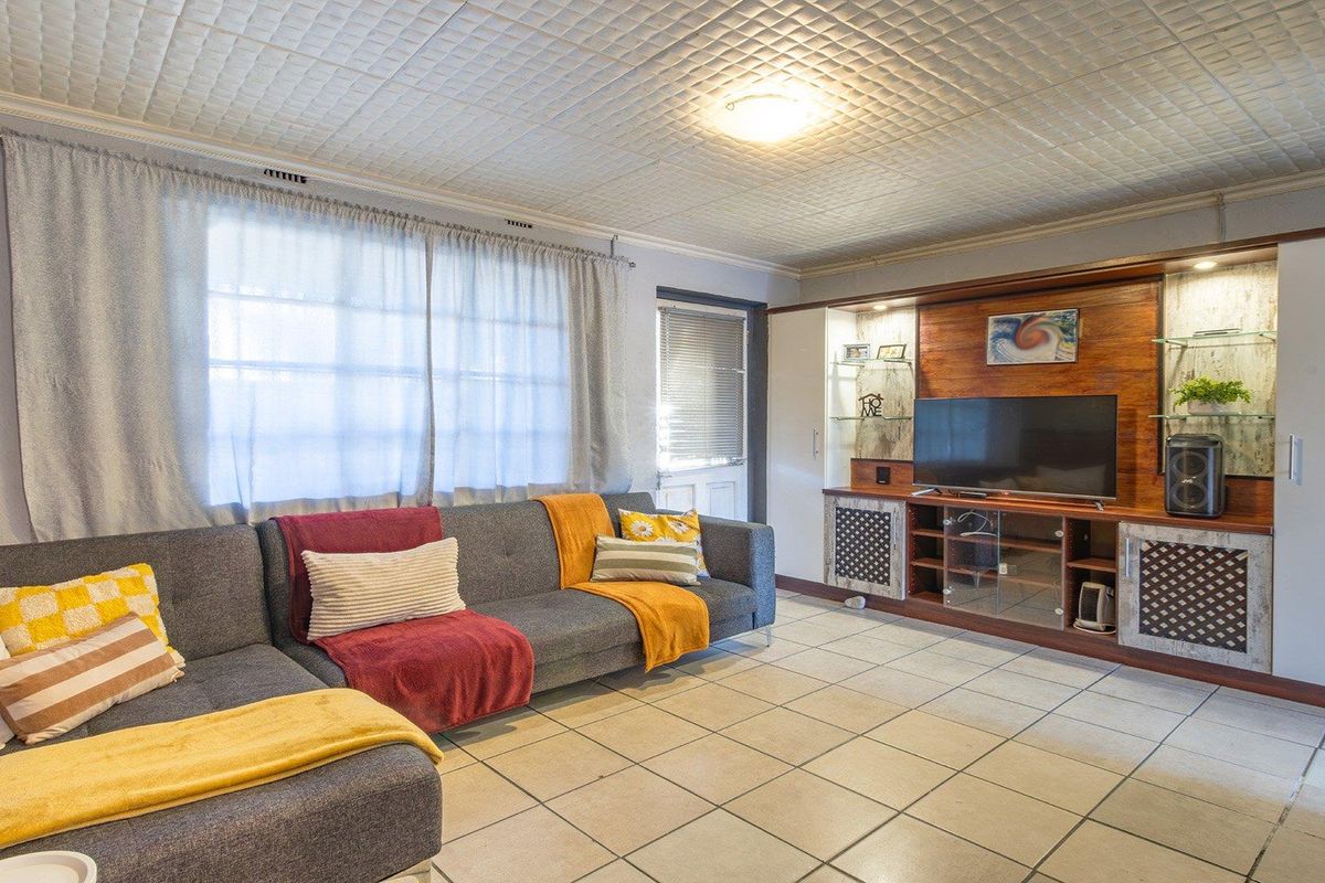 Spacious living room featuring tiled flooring, a built-in wooden entertainment unit with integrated shelving, and a textured ceiling finish.