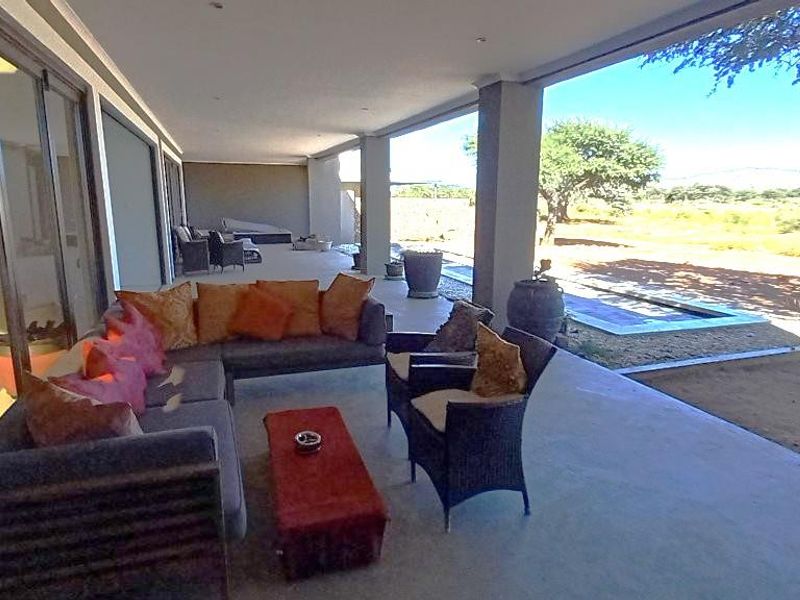 A spacious covered patio featuring concrete flooring and large sliding glass doors, offering an expansive view of the surrounding landscape.