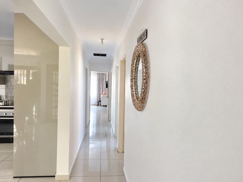 A bright, tiled hallway providing access to multiple rooms, featuring clean white walls and a ceiling access point.