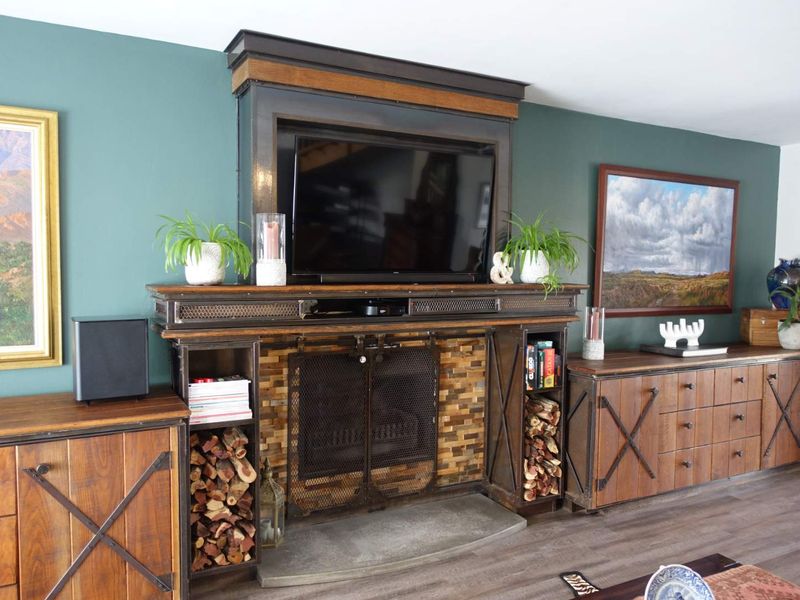 A cozy living room featuring a prominent built-in fireplace with stone detailing, integrated shelving, and wood-look laminate flooring.