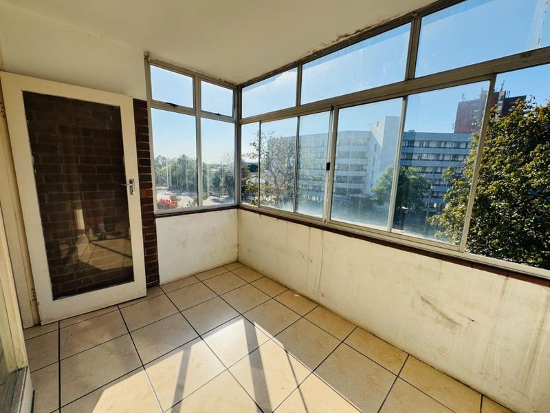An enclosed balcony featuring tiled flooring, large aluminium-framed windows, and brick accents, offering an open view of the surrounding urban area.