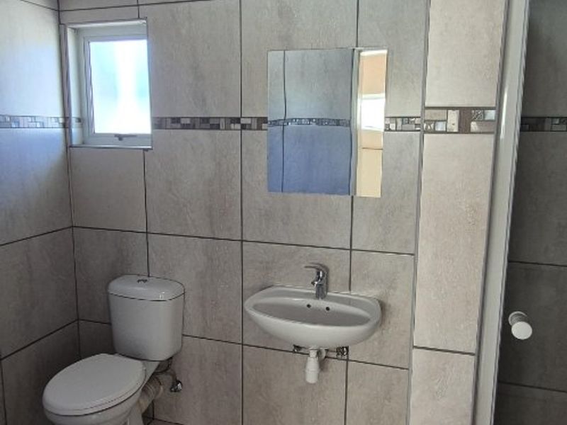 A functional bathroom featuring tiled walls and flooring, a wall-mounted basin, a toilet, and a separate shower enclosure with a timber ceiling.