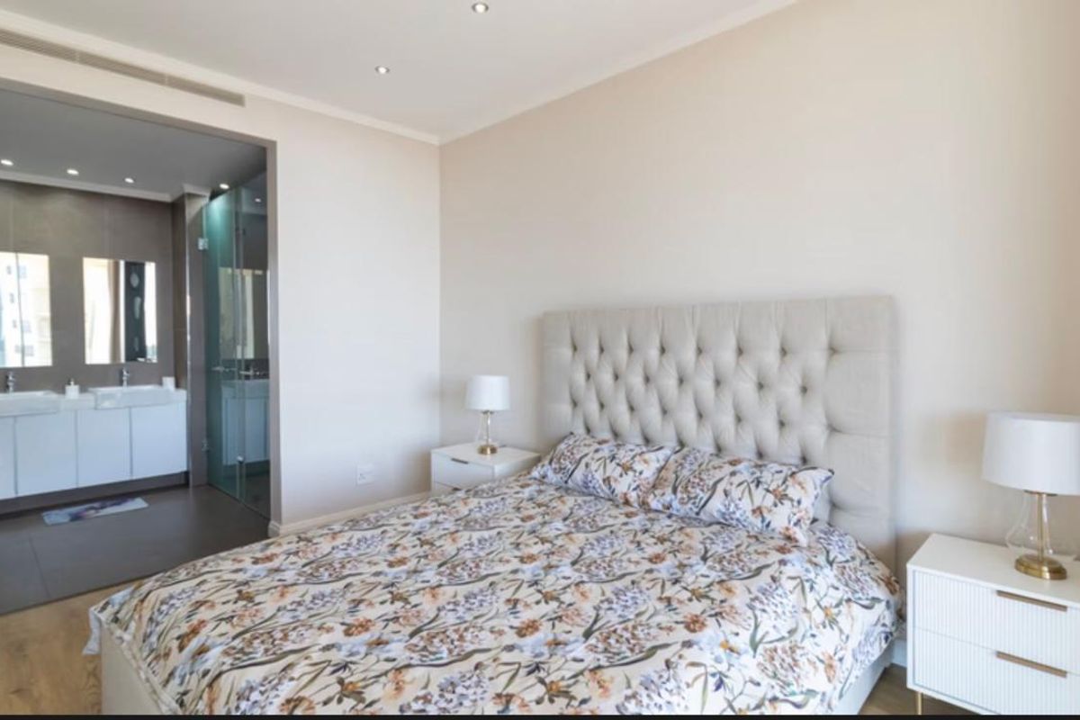 Spacious bedroom featuring laminate flooring, recessed lighting, and an open-plan en-suite bathroom with a modern double vanity and glass shower enclosure.