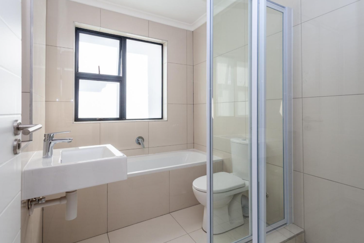A modern bathroom featuring a wall-mounted basin, a built-in bathtub, a toilet, and a glass-enclosed shower with neutral floor-to-ceiling tiling.