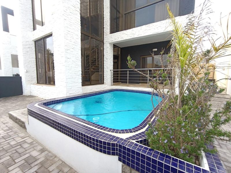 A modern outdoor pool area featuring a tiled swimming pool, stone-clad exterior walls, and a stainless steel balustrade leading to a patio.
