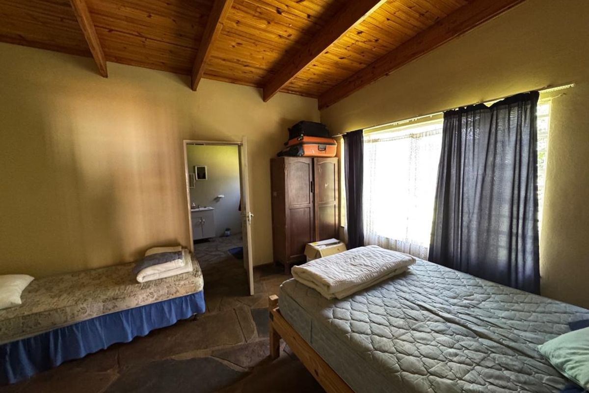 A rustic bedroom featuring exposed timber beam ceilings, natural stone flooring, and an adjoining bathroom entrance.
